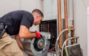 Technician in red gloves inspecting the interior components of a furnace unit during a heating system inspection.