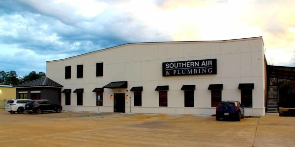 Modern commercial building with cream-colored facade and black awnings displaying Southern Air & Plumbing signage, with parked vehicles in front.